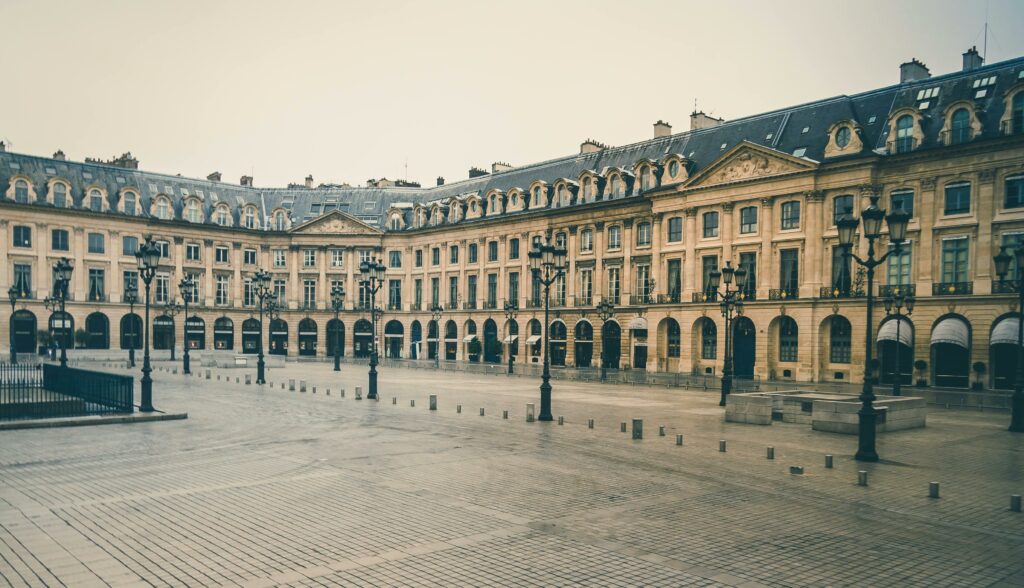 Wide view of an empty European square featuring classic French architecture and ornate street lamps.